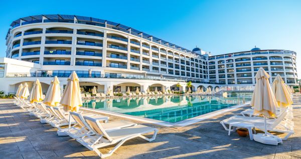 Das Side Moon Palace ist ein modernes Hotel mit mehreren Etagen und Balkonen, von denen aus man den Blick auf einen großzügigen Außenpool genießen kann, der von Reihen weißer Liegestühle und geschlossenen Sonnenschirmen gesäumt ist.