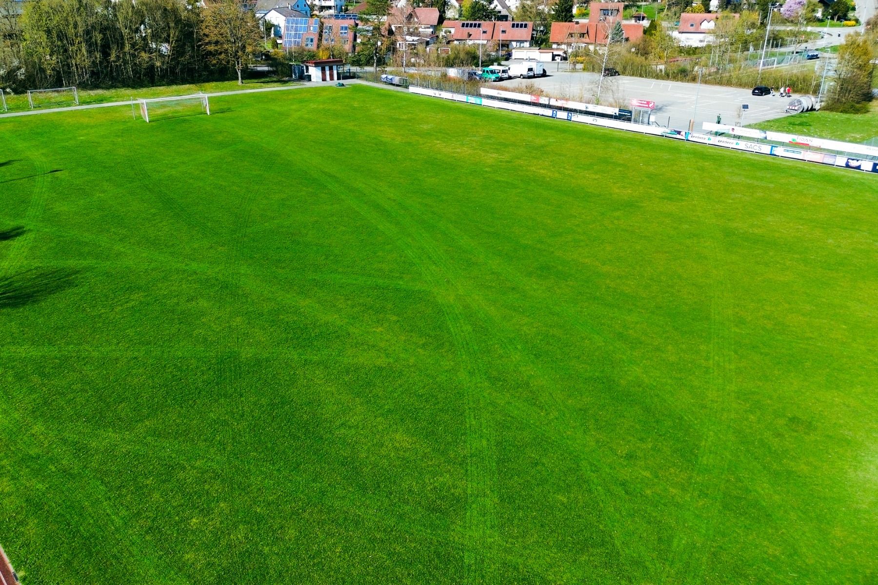 Flyfoto av den store, grønne fotballbanen ved Hotel Empfinger Hof, som er ideell for en fotballtreningsleir, med mål i begge ender og omgitt av trær og bygninger.