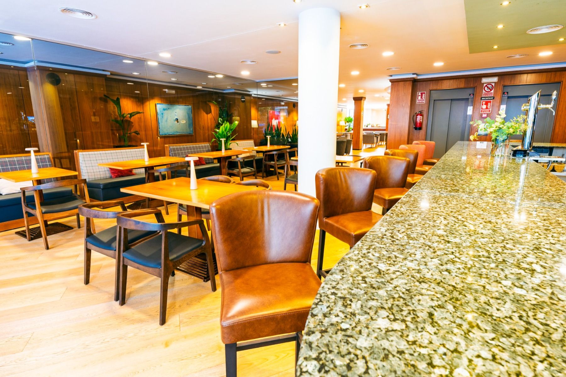 Das hell beleuchtete, moderne Restaurant im Hotel Borgia *** in Gandía ist mit braunen Ledersesseln, Holztischen, Grünpflanzen und einer Theke aus poliertem Stein ausgestattet. Der Raum besticht durch Holzböden und -wände, große Fenster und eine einladend