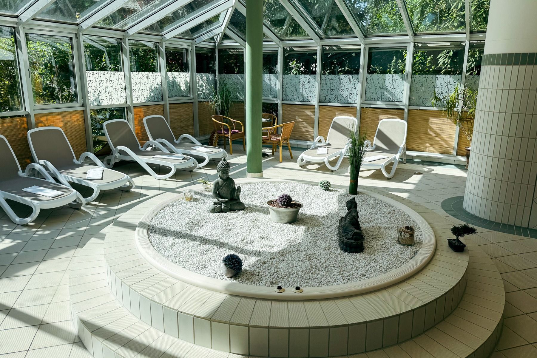 Das Hotel Schloss Schweinsburg verfügt über einen sonnendurchfluteten Wellnessbereich im Innenbereich mit Liegestühlen, die um einen kreisförmigen Zen-Garten mit weißen Kieselsteinen, Statuen und Pflanzen angeordnet sind. Glaswände und eine Glasdecke sorg