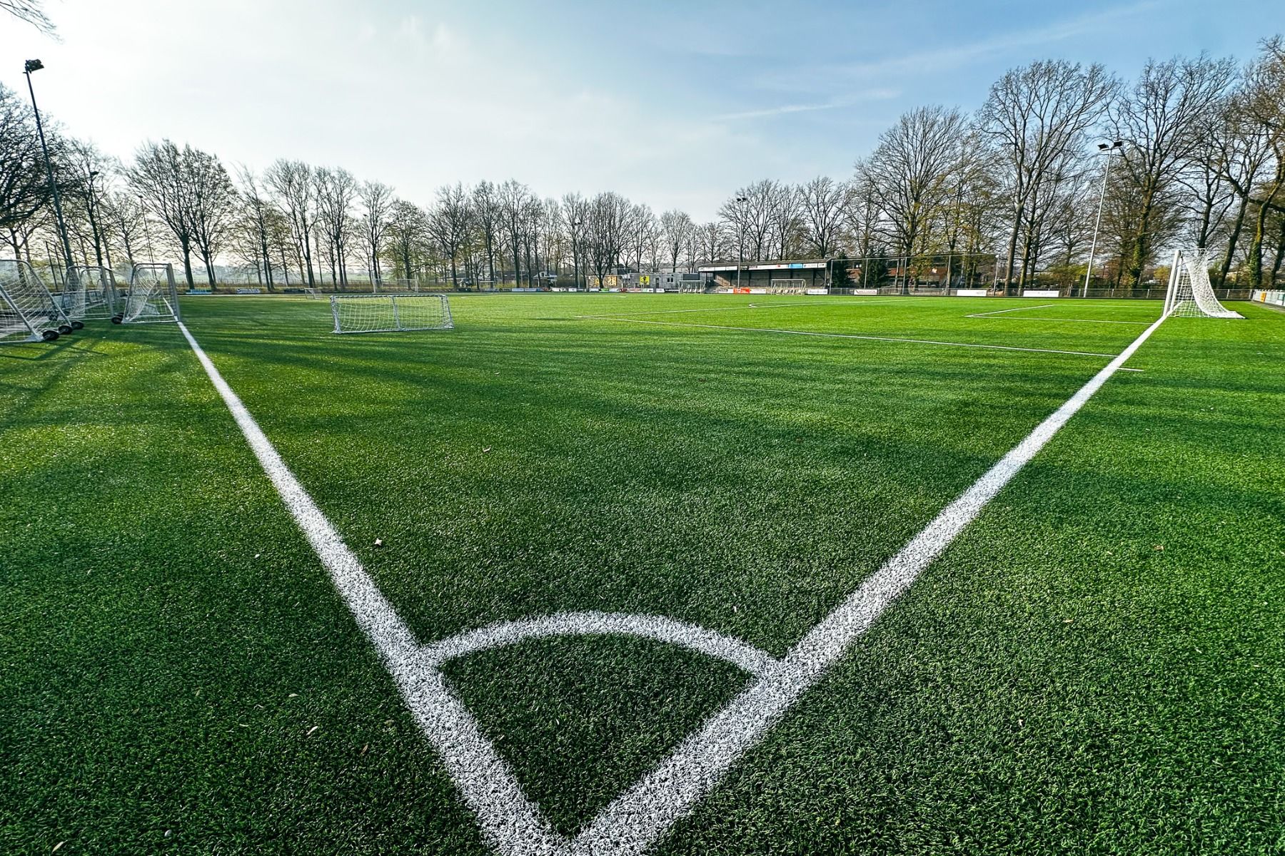 Ein grüner Fußballplatz mit weißen Linien, leeren Toren und Bäumen im Hintergrund unter blauem Himmel im Watersley Sports & Talentpark, der ideale Trainingsmöglichkeiten bietet.