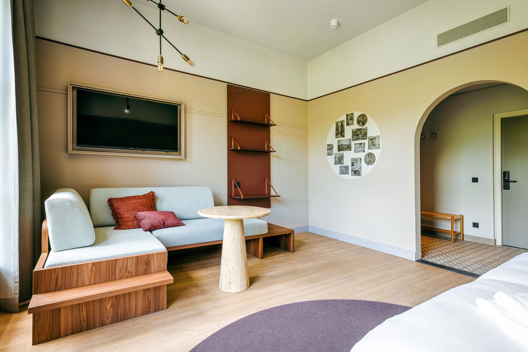 Modernes Hotelzimmer mit Holzboden, blauem Sofa mit roten Kissen, Marmortisch, TV und dekorativen Regalen - ein idealer Aufenthalt im Watersley Sports & Talentpark in der Nähe des Sportcampus Sittard mit einfachem Zugang zu den Trainingseinrichtungen.