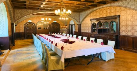 Das Hotel Schloss Schweinsburg ist ein prächtiges historisches Herrenhaus mit rotem Ziegeldach und großen Fenstern, das einen Blick auf gepflegte Gärten mit einem rechteckigen Teich, Hecken, Bänken, hohen Bäumen und nahegelegene Sportplätze bietet, auf de