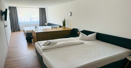 Das Hotel Stadt Mühlhausen*** besticht durch seine weiße Fassade im Industrial-Stil mit großen Fenstern. Ein Schild über dem Eingang weist auf das Hotel hin, das von Bäumen und einem bewölkten Himmel umgeben ist – ideal für Gäste des Trainingslagers oder