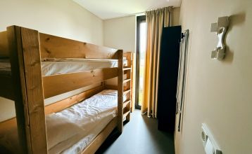 Im Resort De Parel öffnen sich moderne Holzkabinen mit großen Glastüren zu einem Deck mit Stühlen, einem Tisch und einem weißen Sonnenschirm - perfekt für Teambuilding oder Trainingslager im Grünen und ähnliche Kabinen unter teilweise bewölktem Himmel.