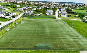 Das Hotel Galántha ist ein modernes, mehrstöckiges Hotel in der Nähe des Schlosses Esterházy, mit großen Glasfenstern und Balkonen, umgeben von Bäumen und einer Straße, mit einem Eingangstor mit Steinsäulen im Vordergrund.