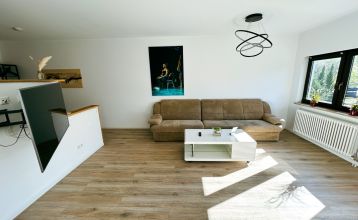 Ein heller Raum im Sportpark Fun4You ist mit runden und rechteckigen Tischen, schwarzen Stühlen, großen Fenstern, einem an der Wand montierten TV-Projektor und einem "Bundesliga"-Schild ausgestattet. Mit Blick auf den Sportplatz ist er perfekt für Teambui