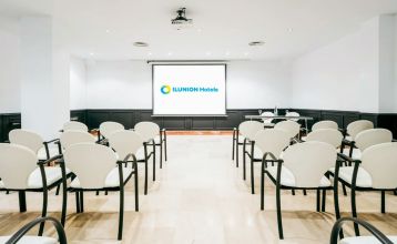 Inngangen til Hotel ILUNION Bel Art Barcelona har store glassdører, potteplanter og et skilt over den svarte markisen - perfekt for gjester som vil utforske Fußballkultur Barcelona eller besøke Trainingseinrichtungen i nærheten.