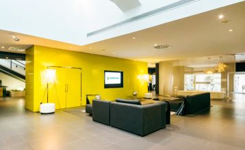 Inngangen til Hotel ILUNION Bel Art Barcelona har store glassdører, potteplanter og et skilt over den svarte markisen - perfekt for gjester som vil utforske Fußballkultur Barcelona eller besøke Trainingseinrichtungen i nærheten.