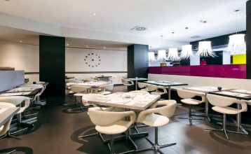 Inngangen til Hotel ILUNION Bel Art Barcelona har store glassdører, potteplanter og et skilt over den svarte markisen - perfekt for gjester som vil utforske Fußballkultur Barcelona eller besøke Trainingseinrichtungen i nærheten.