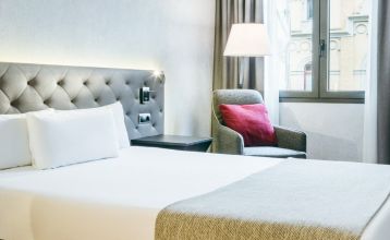 Inngangen til Hotel ILUNION Bel Art Barcelona har store glassdører, potteplanter og et skilt over den svarte markisen - perfekt for gjester som vil utforske Fußballkultur Barcelona eller besøke Trainingseinrichtungen i nærheten.