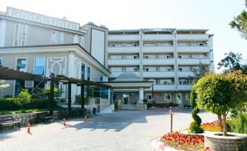Das Linda Resort ist ein mehrstöckiges Hotel mit Blick auf einen Außenpool, der mit Liegestühlen, Sonnenschirmen und Palmen unter strahlend blauem Himmel ausgestattet ist.