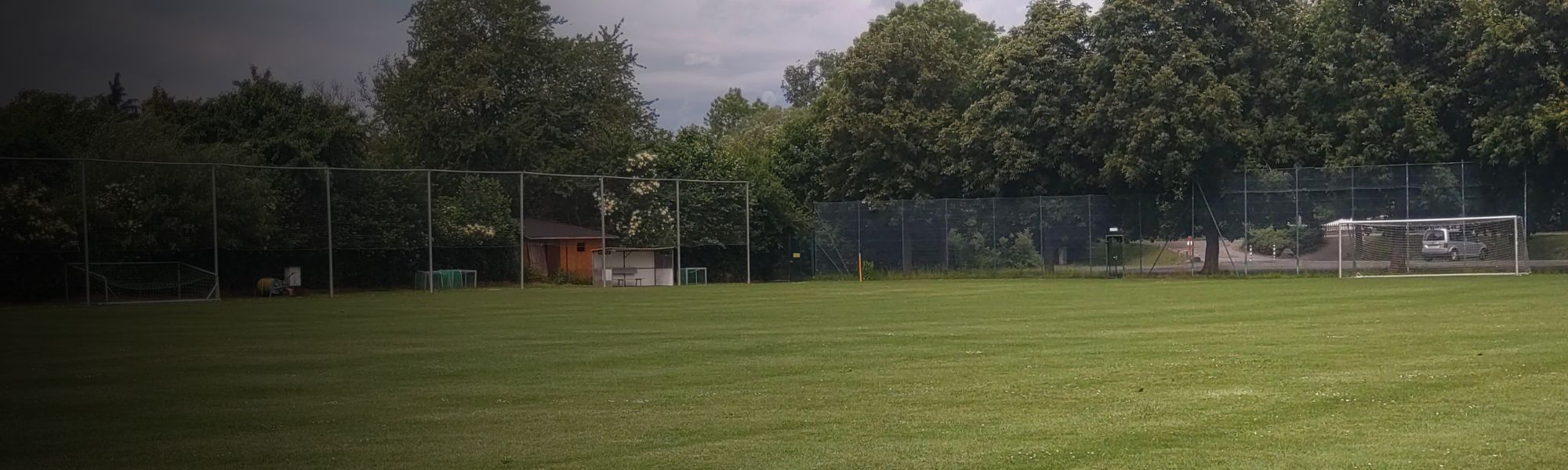 Kunstrasen-Fußballplatz auf Sardinien mit markierten Spielfeldlinien und Umzäunung, im Hintergrund Berge und Gebäude.