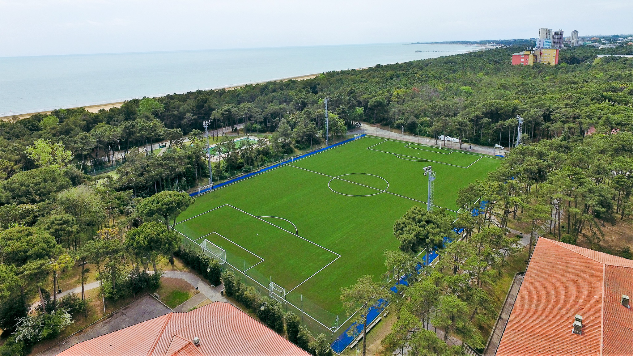 Fußballtrainingsanlage an der Oberen Adria mit Kunstrasenplatz, umgeben von Bäumen und nahe dem Strand.