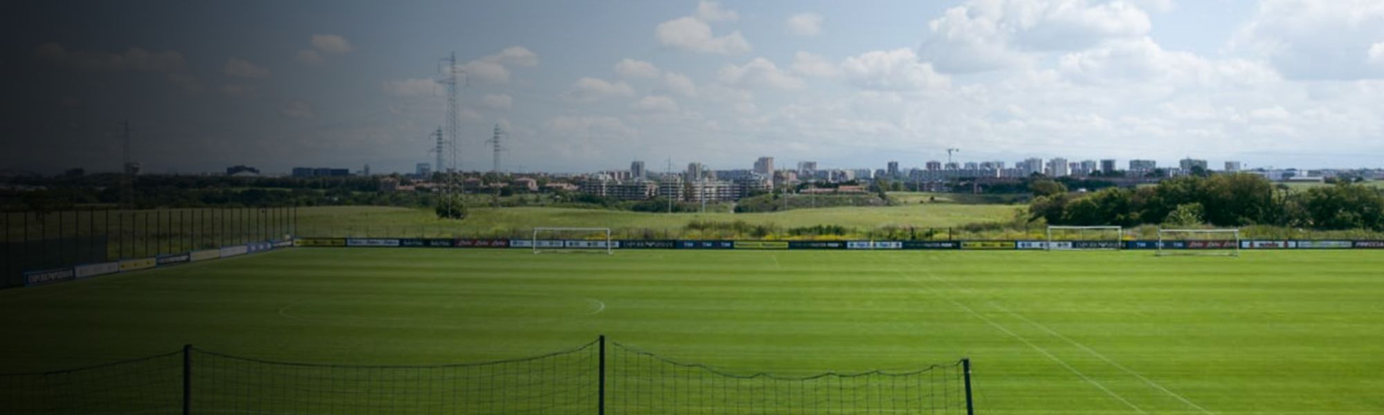 Kunstrasen-Fußballplatz auf Sardinien mit markierten Spielfeldlinien und Umzäunung, im Hintergrund Berge und Gebäude.
