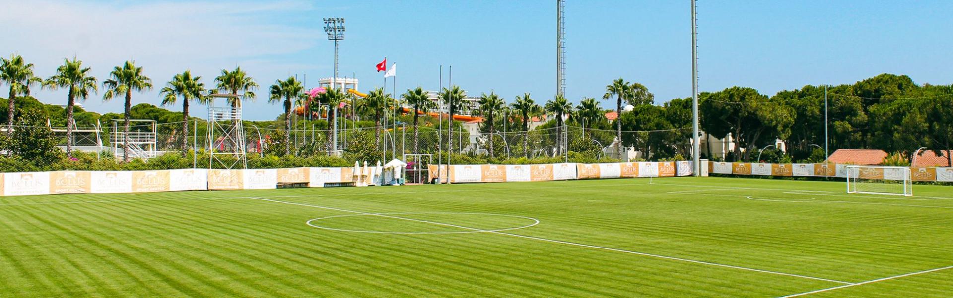 Ein perfektes Fu&szlig;ballfeld in Belek, umgeben von Palmen und Flutlichtmasten.