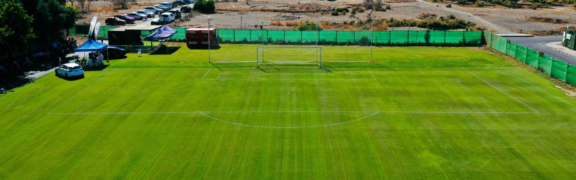 Ein idyllisches Spielfeld mit Naturrasen, eingerahmt von Palmen und weiten Landschaften.