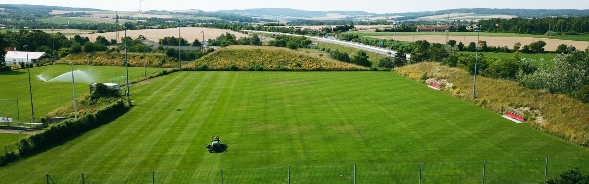 Fu&szlig;balltrainingsplatz in Nieder&ouml;sterreich, eingebettet in eine l&auml;ndliche Landschaft mit Blick auf Felder, Windr&auml;der und eine Landstra&szlig;e.