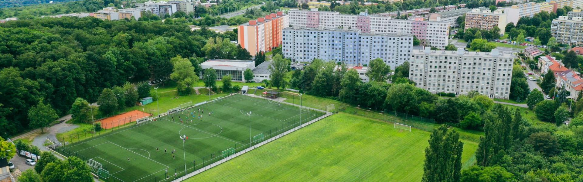 Fu&szlig;ballplatz inmitten einer gr&uuml;nen Landschaft mit Blick auf eine Stadt mit vielen Hochh&auml;usern.