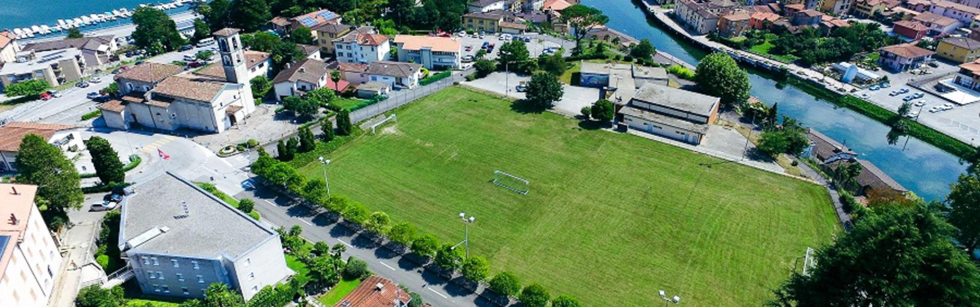 Fu&szlig;ballplatz in der Schweiz, umgeben von H&auml;usern und einem Fluss, mit Blick auf den See.