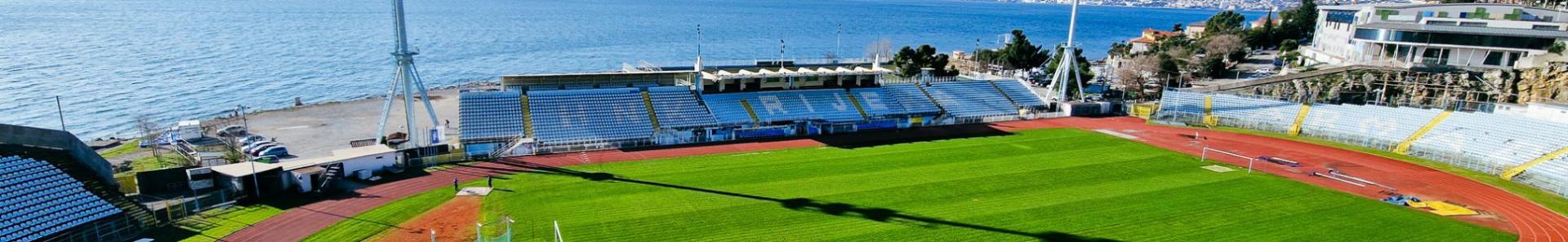 Luftaufnahme eines Fu&szlig;ballstadions an der Kvarner Bucht in Kroatien, direkt am Meer gelegen, mit Laufbahn und Trib&uuml;nen, umgeben von Bergen und der Adria im Hintergrund.