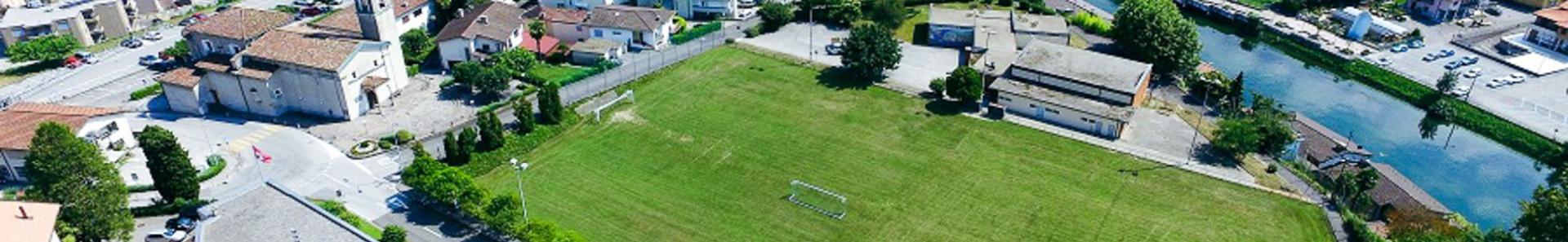Fu&szlig;ballplatz in der Schweiz, umgeben von H&auml;usern und einem Fluss, mit Blick auf den See.