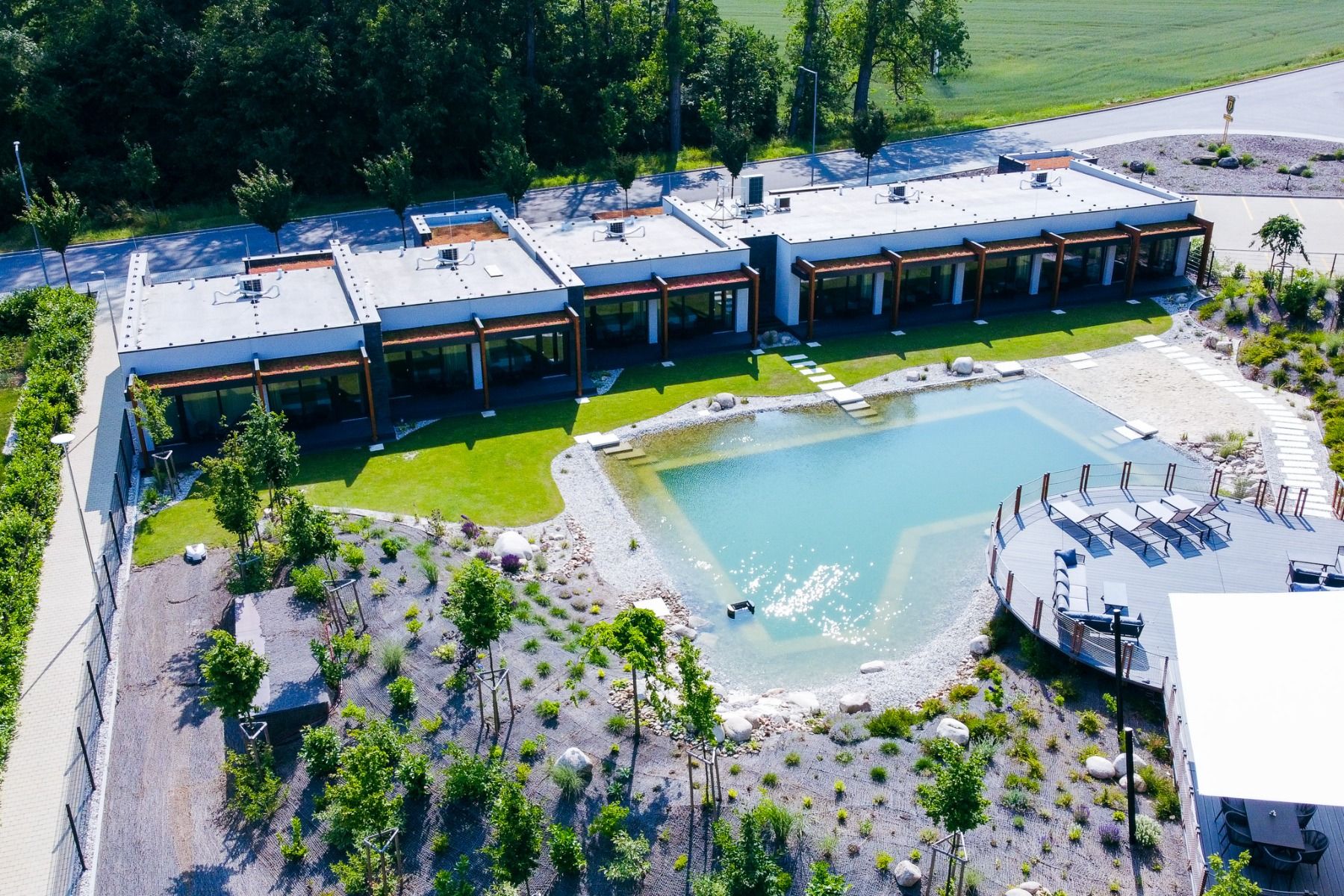Ein moderner Komplex mit Flachdach und großzügigen Fensterfronten – das Hotel Jagdfestung – bietet einen Blick auf einen wunderschön angelegten Teich und Garten. Umgeben von üppigem Grün und gewundenen Wegen, wie von oben zu sehen ist, bietet es den ideal