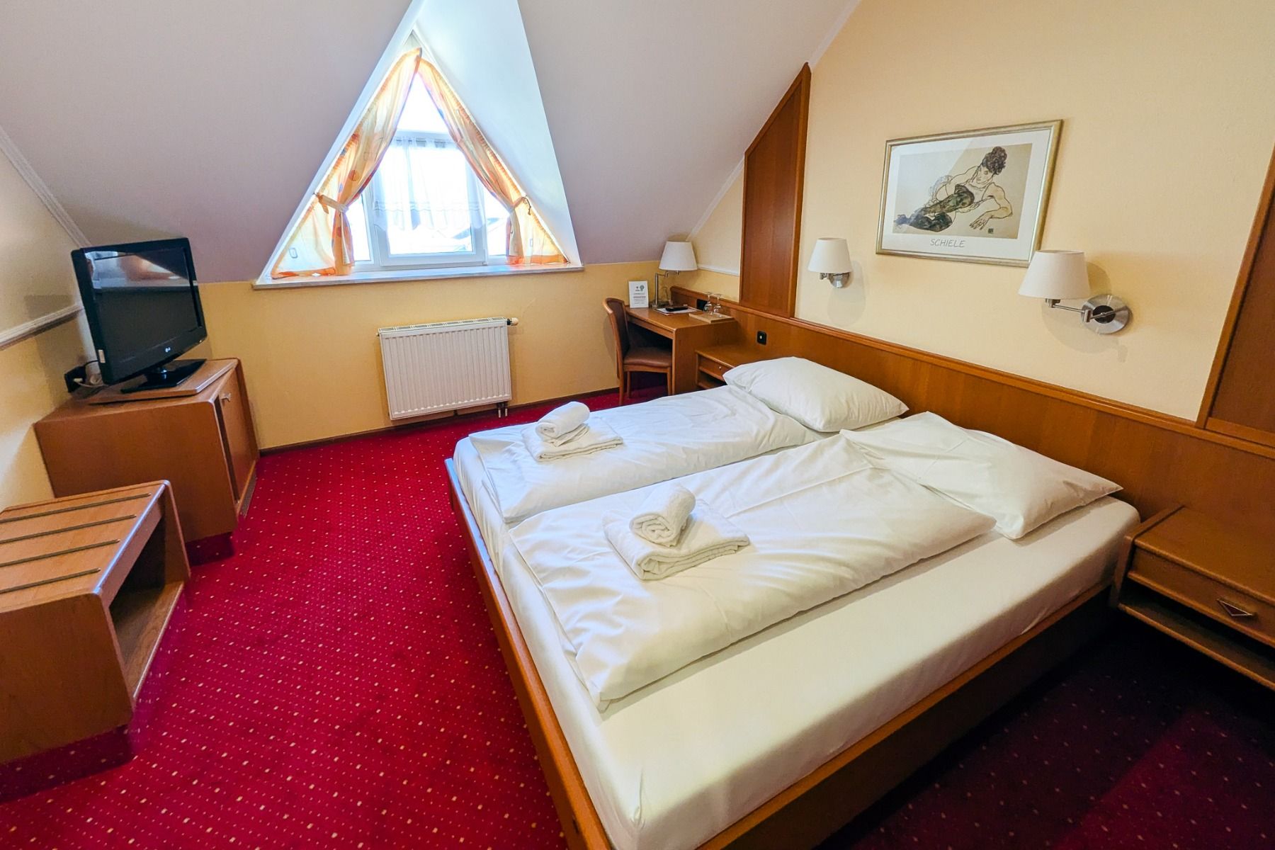 Das Hotel Restaurant Schachenwald bietet ein gemütliches Zimmer mit einem Doppelbett, weißer Bettwäsche, Holzmöbeln und einem Flachbildfernseher – ideal zum Entspannen nach einem Tag am Schwarzlsee oder nach dem Training auf dem Indoor-Kunstrasenplatz.