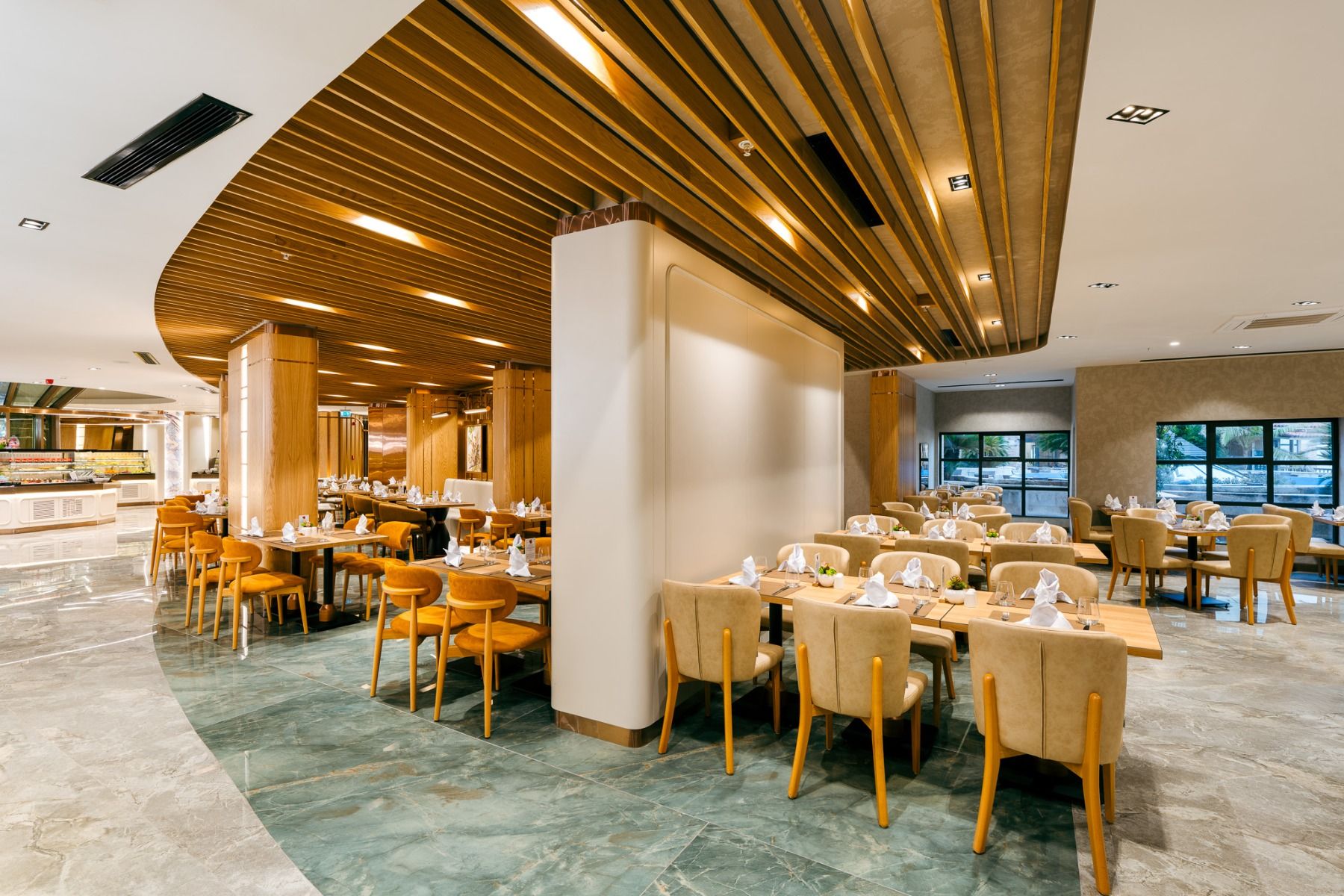 Das Hotel Limak Arcadia bietet ein modernes, geräumiges Restaurant mit Holztischen und -stühlen, eleganter Einrichtung und großen Fenstern - ein einladender Ort, der sich perfekt für ein Fußballtrainingslager in der Türkei eignet.