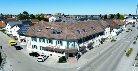 Der Hanauer Hof, ein gro&szlig;es traditionelles Hotel mit Ziegeldach und gr&uuml;nen Fensterl&auml;den, steht an einer Stra&szlig;enecke in Appenweier. Autos sind drau&szlig;en geparkt, Sonnenkollektoren s&auml;umen das Dach, und ein Kunstrasenplatz ist unter dem klaren blauen Himmel ni