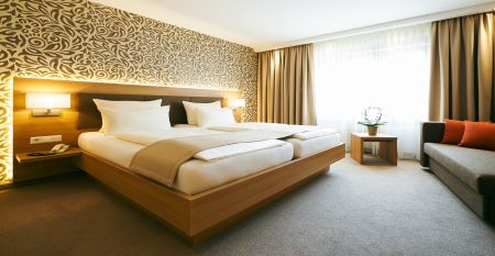 Der Hanauer Hof, ein gro&szlig;es traditionelles Hotel mit Ziegeldach und gr&uuml;nen Fensterl&auml;den, steht an einer Stra&szlig;enecke in Appenweier. Autos sind drau&szlig;en geparkt, Sonnenkollektoren s&auml;umen das Dach, und ein Kunstrasenplatz ist unter dem klaren blauen Himmel ni