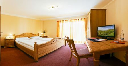 Der Hanauer Hof, ein gro&szlig;es traditionelles Hotel mit Ziegeldach und gr&uuml;nen Fensterl&auml;den, steht an einer Stra&szlig;enecke in Appenweier. Autos sind drau&szlig;en geparkt, Sonnenkollektoren s&auml;umen das Dach, und ein Kunstrasenplatz ist unter dem klaren blauen Himmel ni