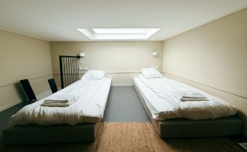 Im Resort De Parel öffnen sich moderne Holzkabinen mit großen Glastüren zu einem Deck mit Stühlen, einem Tisch und einem weißen Sonnenschirm - perfekt für Teambuilding oder Trainingslager im Grünen und ähnliche Kabinen unter teilweise bewölktem Himmel.