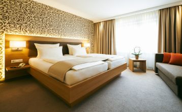 Der Hanauer Hof, ein großes traditionelles Hotel mit Ziegeldach und grünen Fensterläden, steht an einer Straßenecke in Appenweier. Autos sind draußen geparkt, Sonnenkollektoren säumen das Dach, und ein Kunstrasenplatz ist unter dem klaren blauen Himmel ni