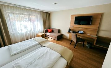 Der Hanauer Hof, ein großes traditionelles Hotel mit Ziegeldach und grünen Fensterläden, steht an einer Straßenecke in Appenweier. Autos sind draußen geparkt, Sonnenkollektoren säumen das Dach, und ein Kunstrasenplatz ist unter dem klaren blauen Himmel ni