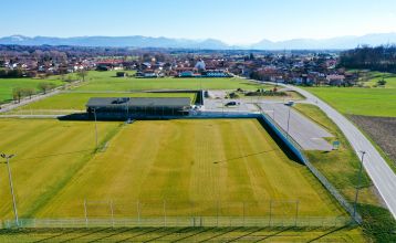 Das Egger Stüberl ist ein weißes, zweistöckiges Gebäude mit rotem Ziegeldach und Balkonen unter strahlend blauem Himmel. Perfekt für Besucher oder Trainingslager in der Nähe lokaler Fußballplätze, bietet es Sitzgelegenheiten im Freien und Pflanzen zur Beg