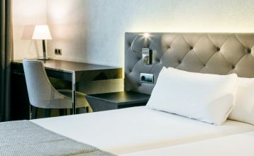 Inngangen til Hotel ILUNION Bel Art Barcelona har store glassdører, potteplanter og et skilt over den svarte markisen - perfekt for gjester som vil utforske Fußballkultur Barcelona eller besøke Trainingseinrichtungen i nærheten.