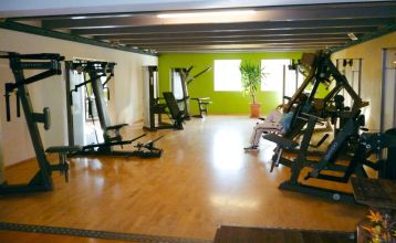 Luftaufnahme des Hotels Drei Rosen in Moosburg an der Isar – ein vierstöckiges, hellviolettes Hotel mit Sonnenkollektoren, Glasbalkonen und einem Außenbereich mit orangefarbenen Tischen und Stühlen, ideal für ein Fußballtrainingslager.