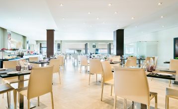 Ein hohes, gelbes Hotel Sol Guadalmar mit Balkonen blickt auf einen klaren, blauen Außenpool, umgeben von Palmen und grünen Rasenflächen unter einem sonnigen Himmel - perfekt für Ihren Aufenthalt in diesem zentrumsnahen 4 Sterne Hotel Malaga.