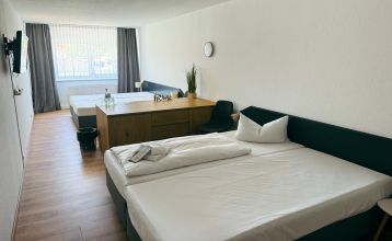 Das Hotel Stadt Mühlhausen*** besticht durch seine weiße Fassade im Industrial-Stil mit großen Fenstern. Ein Schild über dem Eingang weist auf das Hotel hin, das von Bäumen und einem bewölkten Himmel umgeben ist – ideal für Gäste des Trainingslagers oder