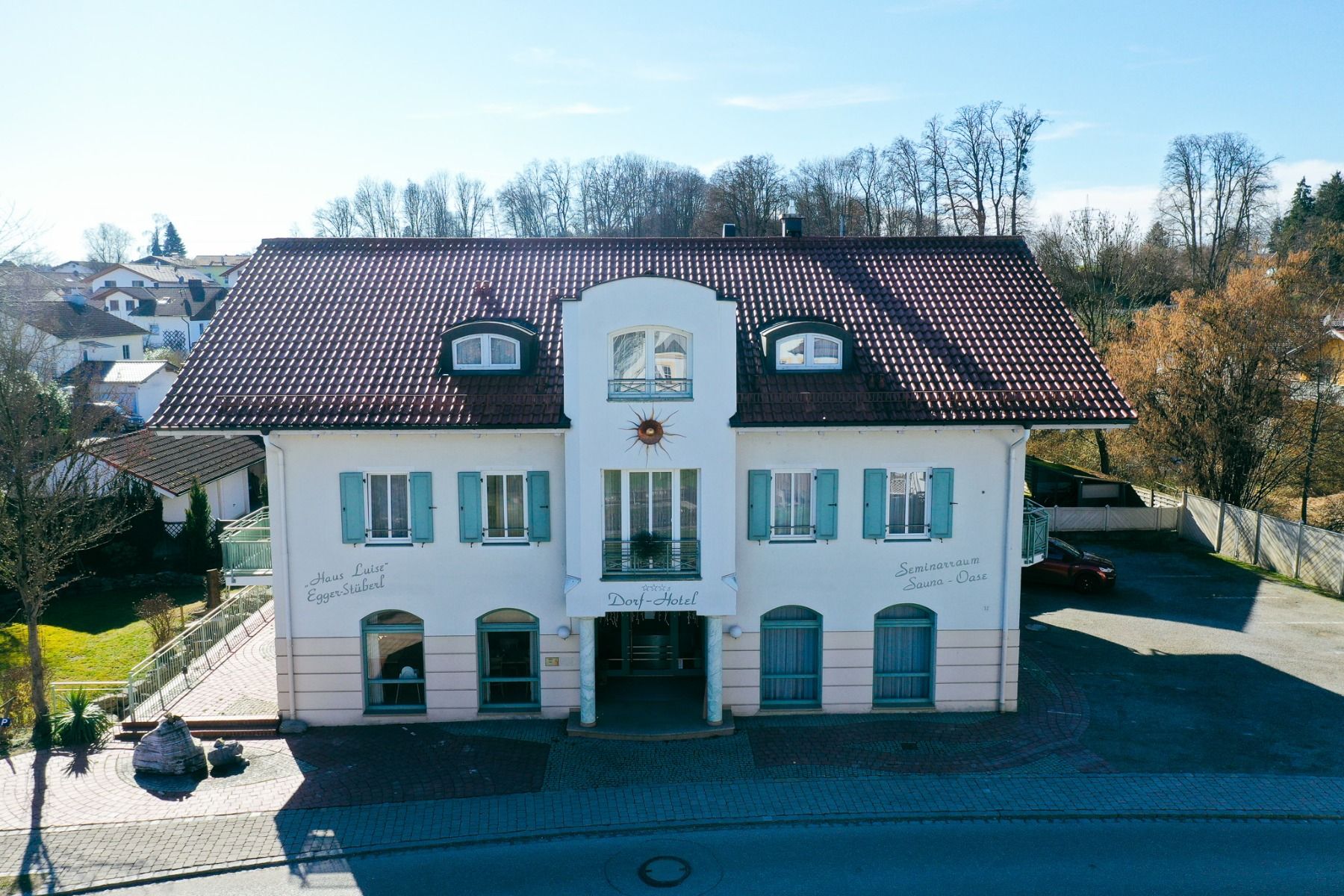 The Egger Stüberl, a white, two-storey building with a red tiled roof, blue shutters and arched windows, is a charming spot near the local soccer pitch - ideal for visitors looking to relax under a blue sky.