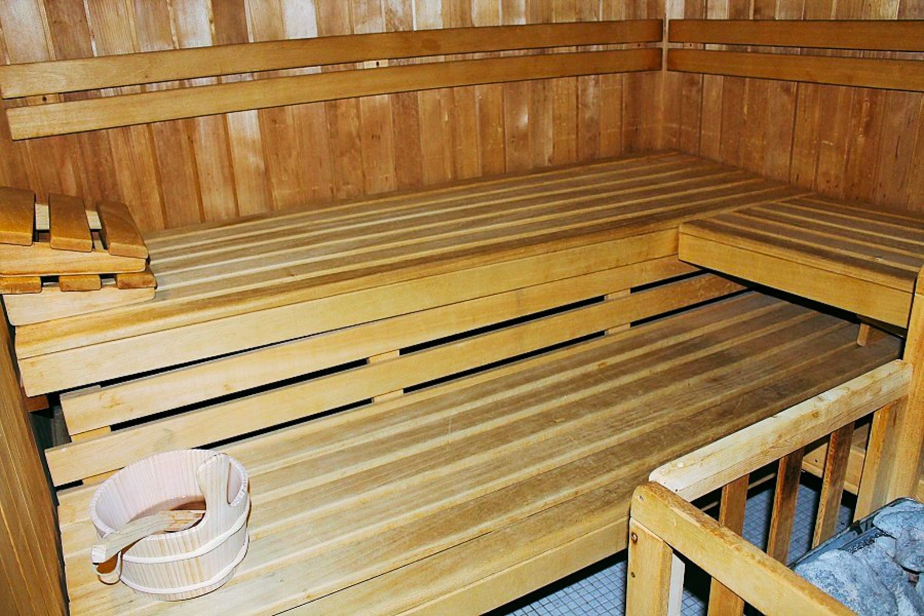A light wood sauna room with tiered benches, bucket and ladle on a clean tile floor - ideal for relaxing in the fitness and wellness area of the Sports & Seminar Center. All walls, benches and accessories are made of light-colored wood.