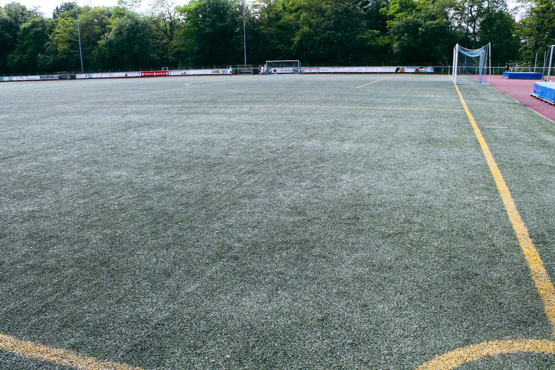 The Sport & Seminar Center features an outdoor soccer field with artificial turf, yellow boundary lines, and a distant goalpost—perfect for fitness and wellness activities. The field is surrounded by trees and a running track.