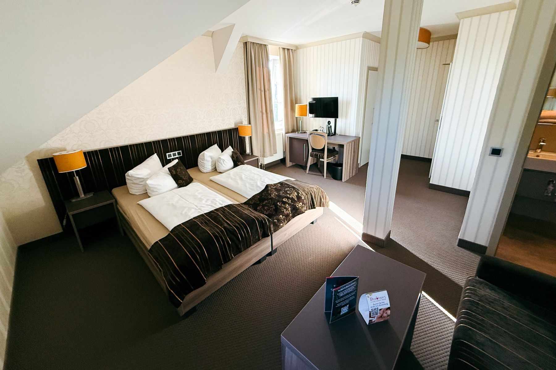 Et hotellrom på Hotel Dorotheenhof med to enkeltsenger, et skrivebord og en stol, en TV, lamper, en sofa og et bad som kan ses gjennom en åpen dør. Innredningen kombinerer moderne stil med historisk sjarm og utmerker seg med nøytrale farger og stripete se