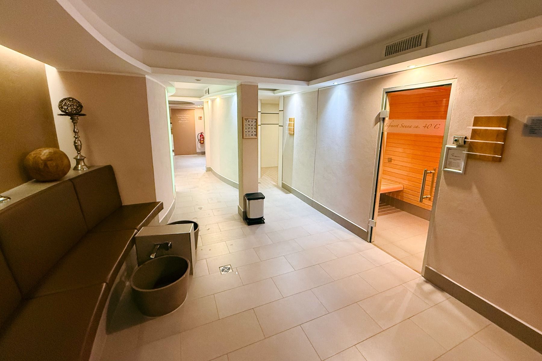 The well-maintained wellness area at the Hotel Dorotheenhof features beige walls, a bench, decorative elements, and a door leading to the sauna. Through the glass door, you can see inside the sauna and the wooden benches, creating a warm and inviting atmo