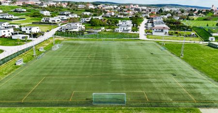 Hotel Gal&aacute;ntha, a modern multi-story hotel with expansive glass windows and a rooftop terrace, stands on a street corner in Burgenland amidst trees and historic stone pillars, echoing the elegance of Esterh&aacute;zy Palace.