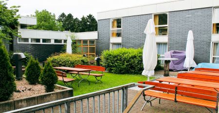 Exterior view of the modern sports and seminar center with HOSTEL sign, concrete staircase, blue accents, yellow wall, art and green areas - an ideal location for training camps with conference rooms nearby.