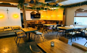 At Resort De Parel, modern wooden cabins with large glass doors open onto a deck with chairs, a table and a white parasol - perfect for team building or training camps in the countryside and similar cabins under partly cloudy skies.