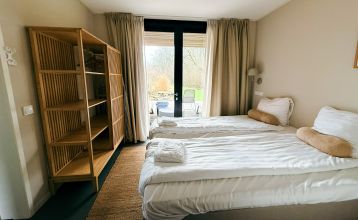 At Resort De Parel, modern wooden cabins with large glass doors open onto a deck with chairs, a table and a white parasol - perfect for team building or training camps in the countryside and similar cabins under partly cloudy skies.