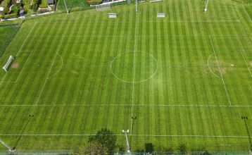 Hotel Galántha, a modern multi-story hotel with expansive glass windows and a rooftop terrace, stands on a street corner in Burgenland amidst trees and historic stone pillars, echoing the elegance of Esterházy Palace.